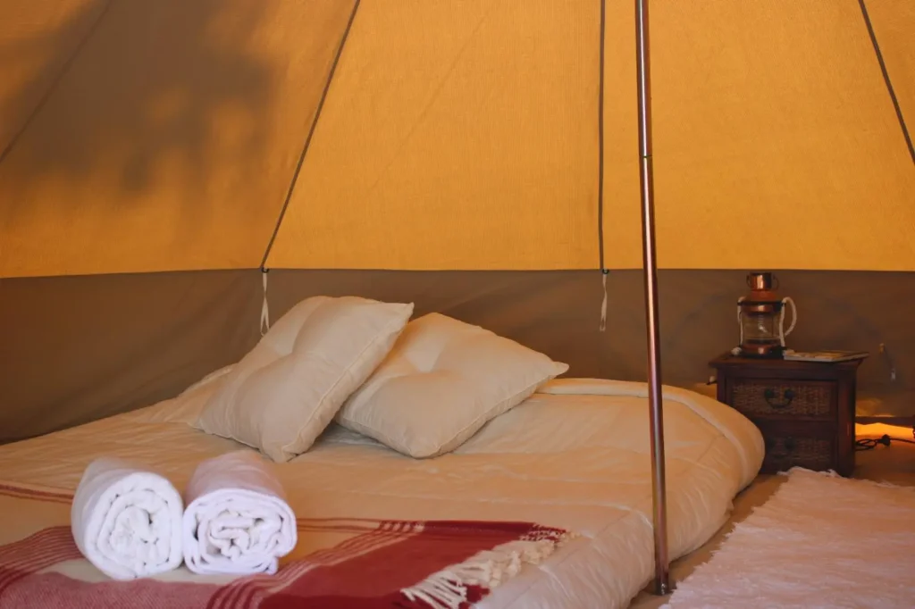 T: Interior de tenda glamping aconchegante com cama de casal e lanterna decorativa no Wild Nature Surf Camp